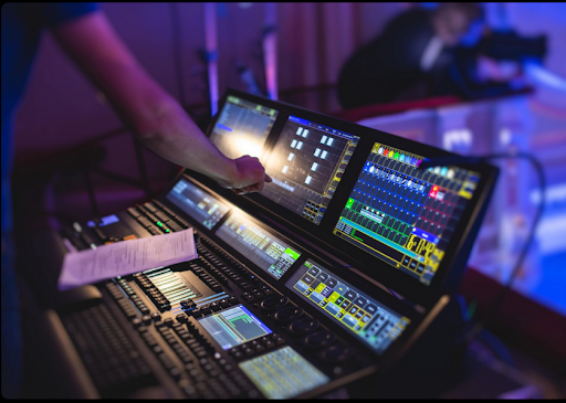 Evelyne Thomas, une femme aux cheveux bruns ondulés mi-longs avec des mèches, sourit. Elle porte un haut et un blazer noirs, se tenant devant des plantes vertes dans un environnement extérieur.