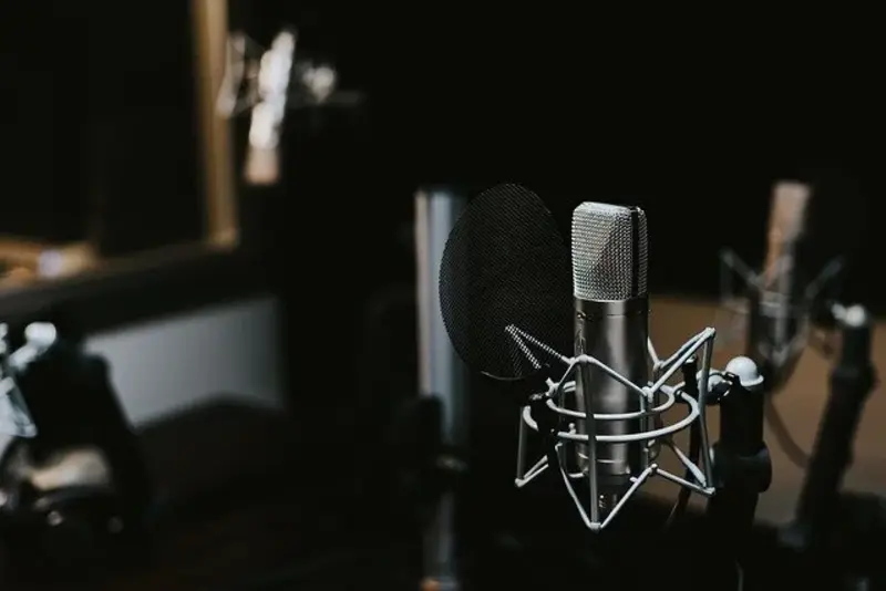 Microphone professionnel avec filtre anti-pop dans un studio d’enregistrement sombre, entouré d’équipements audio flous.